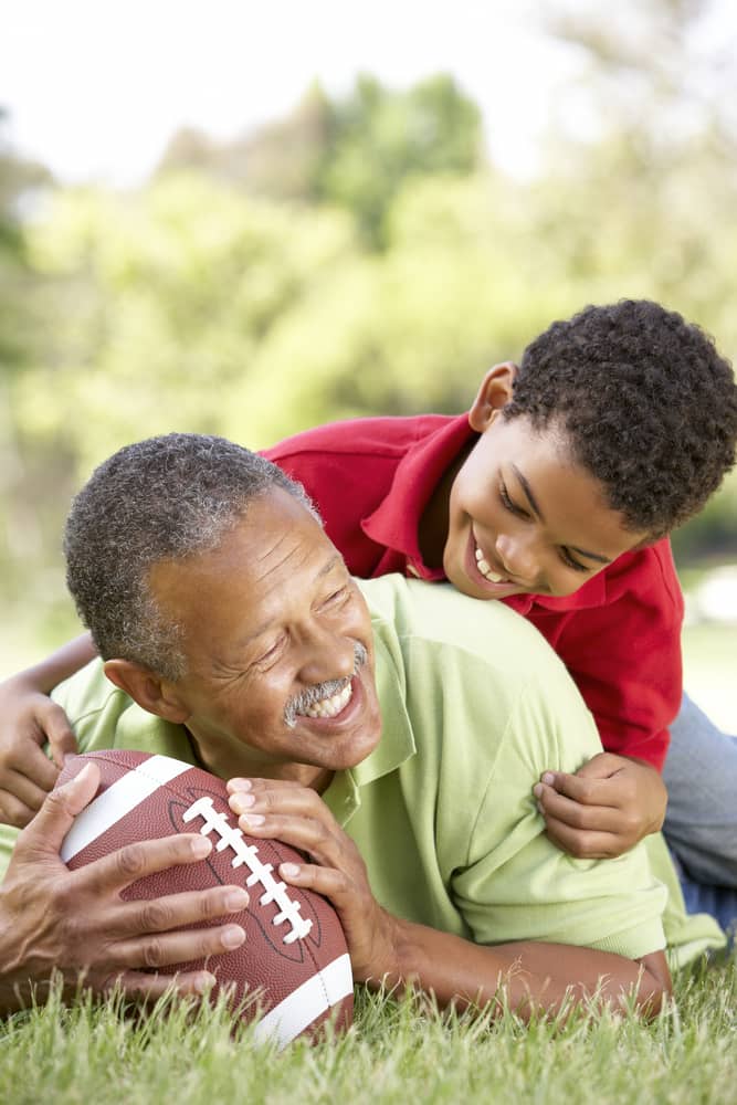 Black grandfather and grandson playing American football.