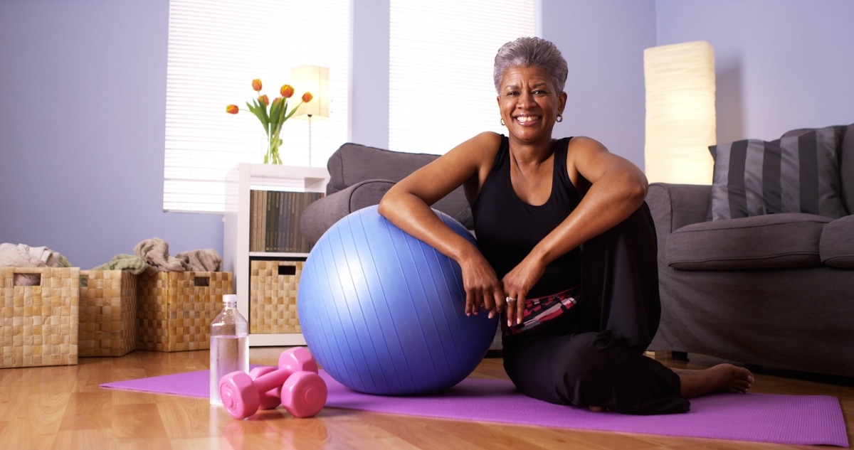 An older woman sitting and smiling next to an exercise ball.