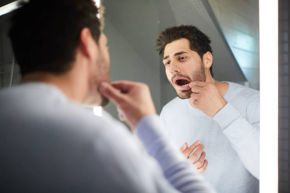 رجل يفحص فمه من الداخل في مرآة الحمام بحثًا عن علامات مشاكل مرض السكري.