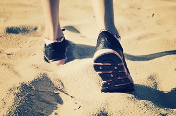 Photo of someone’s feet wearing shoes and walking on the sand.