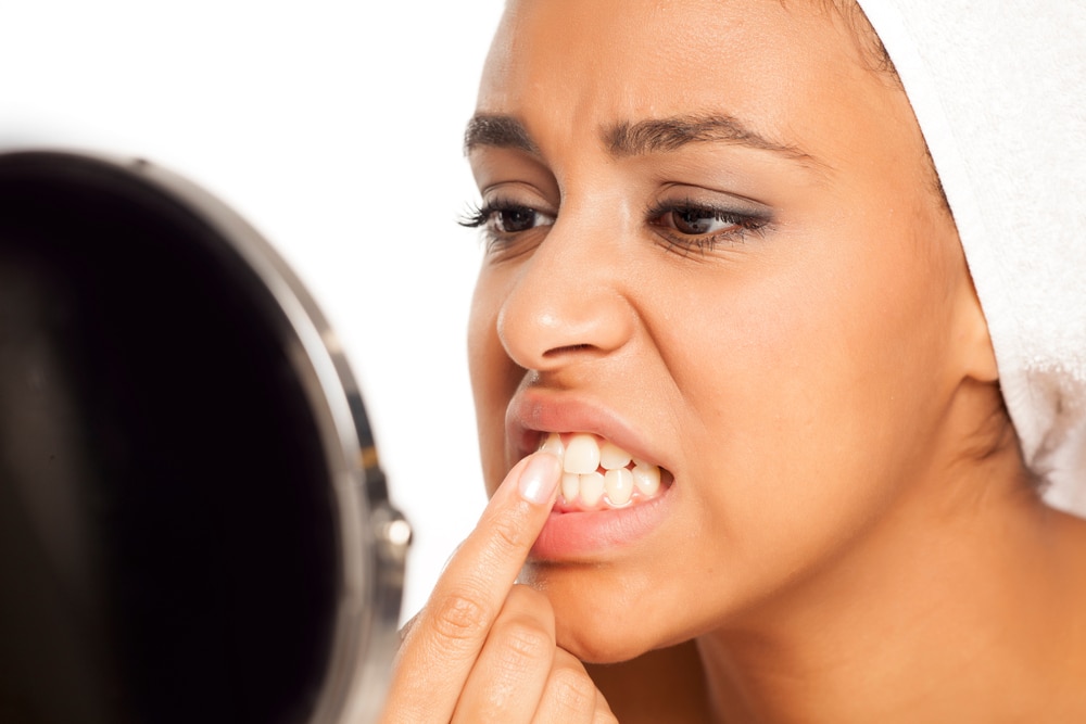 A woman checks her teeth in a mirror.