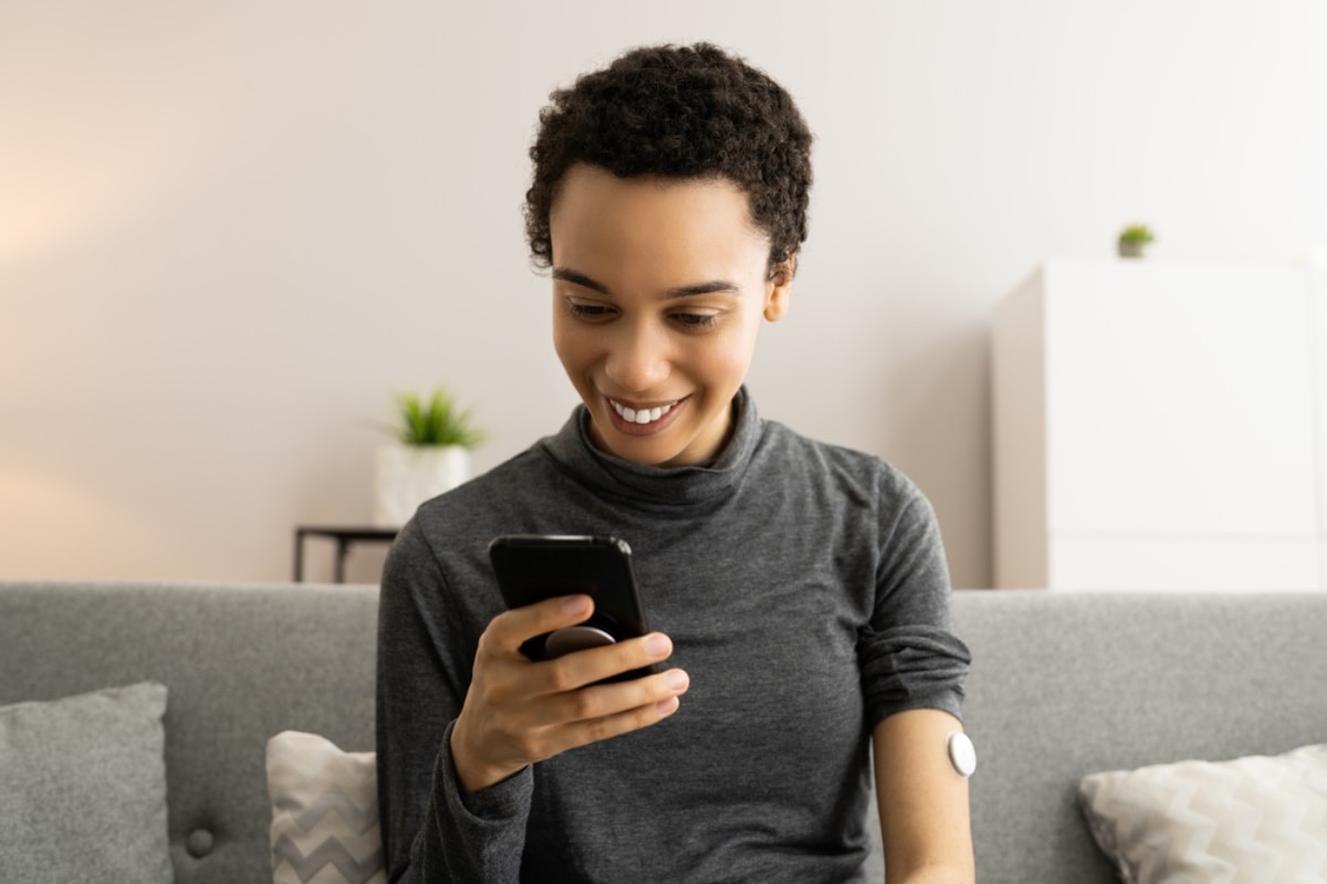 A woman with a continuous glucose monitor on her arm looks at her smartphone to check her glucose level.