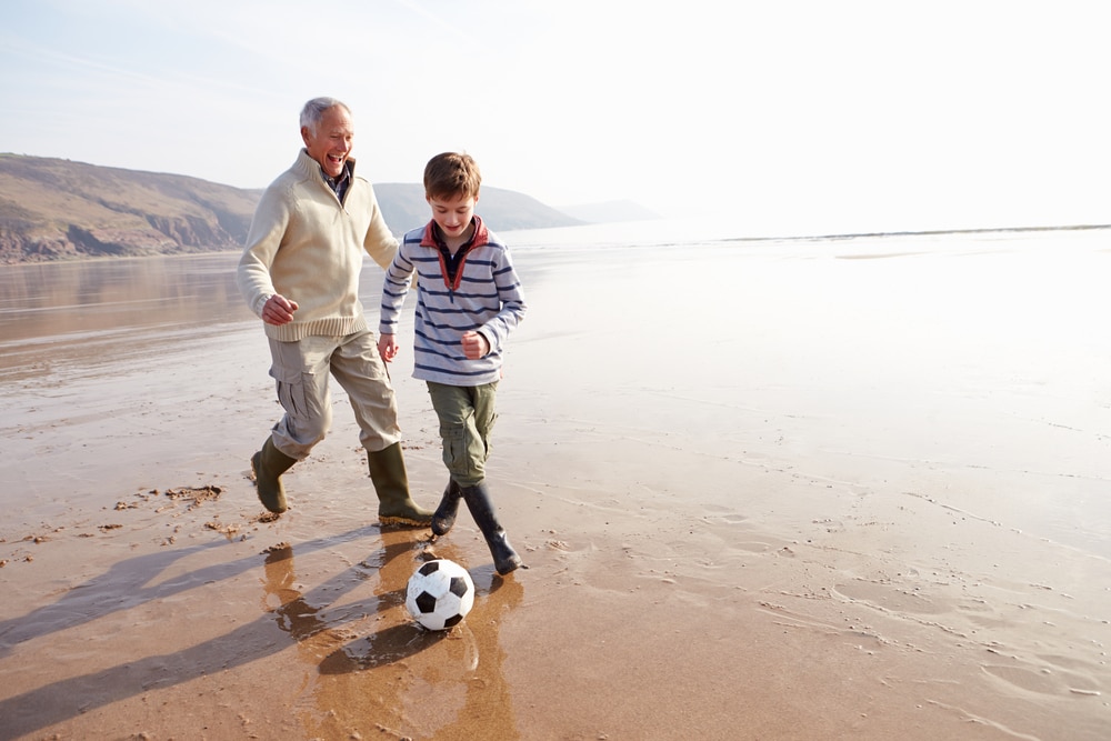 Grandfather playing soccer with his grandson on the beach.