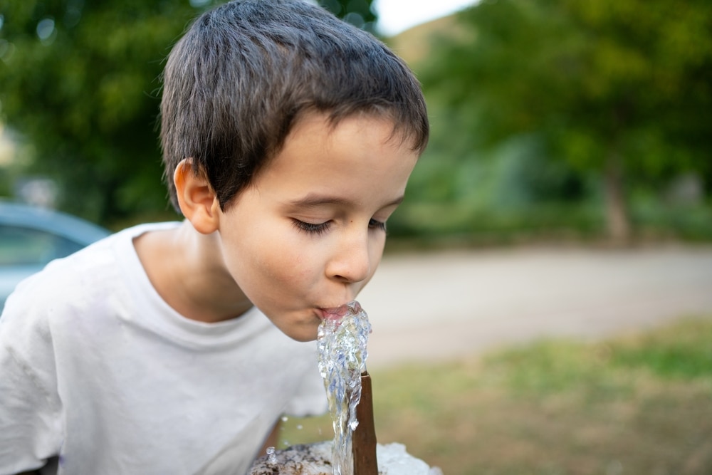 A young boy drinking water from a fountain outdoors.