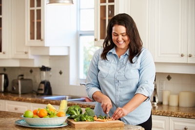 Eine lächelnde junge Frau, die Gemüse in ihrer Küche hackt
