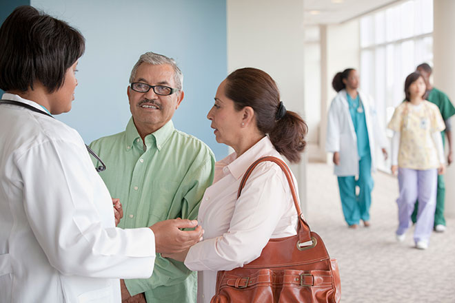 Una profesional de atención médica hablando con un paciente y un familiar del paciente.