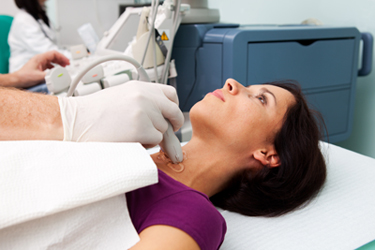 A female patient getting an ultrasound of her thyroid. The transducer is run over her neck for the test.