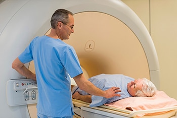 X-ray technician and a man lying on a table that slides into a tunnel-shaped device for an x-ray.