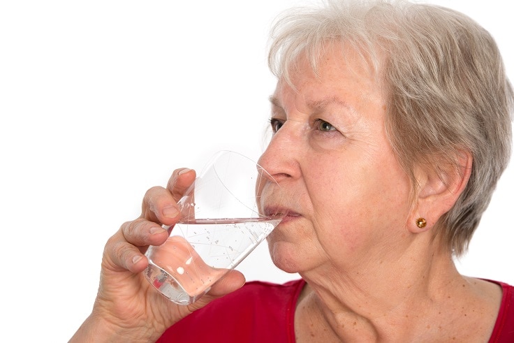 A woman drinking a clear liquid from a glass.