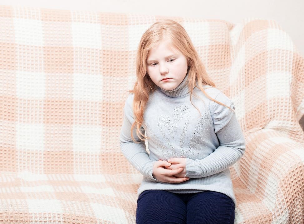 Child sitting on a sofa, holding her abdomen.