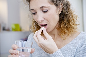 Image of a woman taking medications with a glass of water