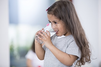 Una niña bebe agua de un vaso.