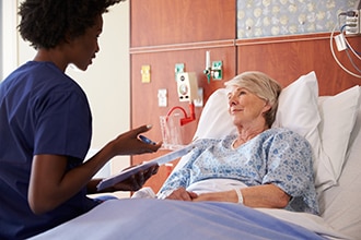 أخصائي رعاية صحية يتحدث مع مريضة مسنة ترقد في سرير المستشفى.