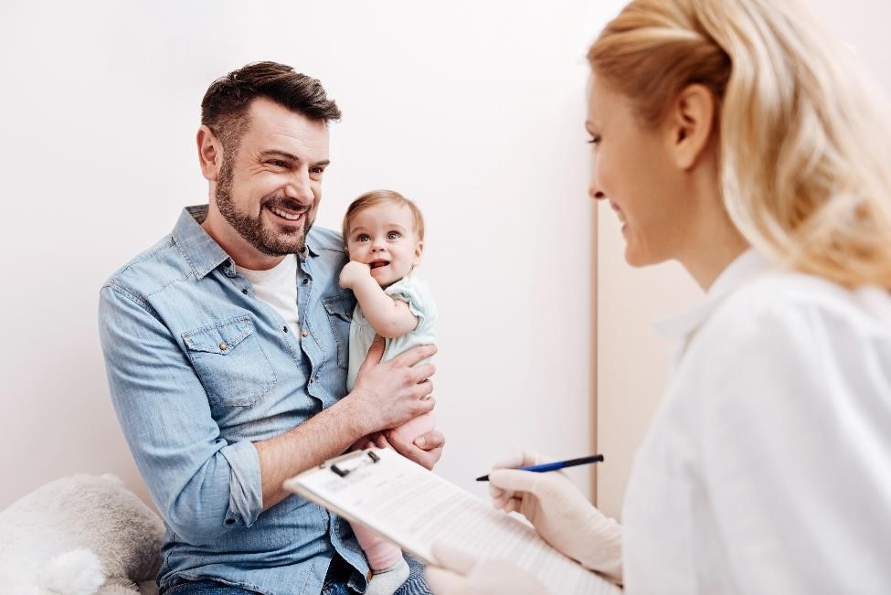 Father holding an infant and talking with a pediatrician.