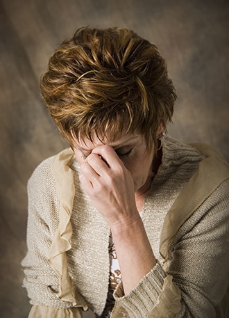 An upset woman with her head down and hand on her forehead.