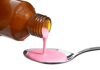 Medicamento líquido de color rosado que está siendo vertido desde un frasco a una cuchara.