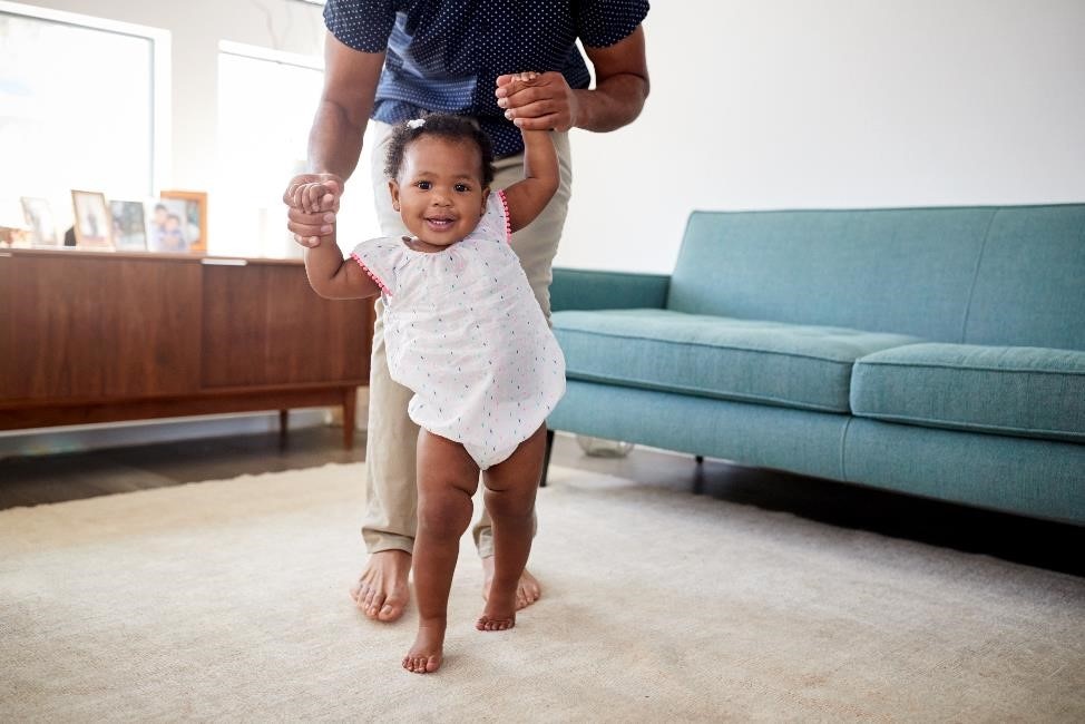 Older infant walking while holding parent’s hands.