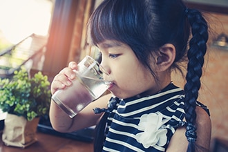 A girl drinks water from a glass.