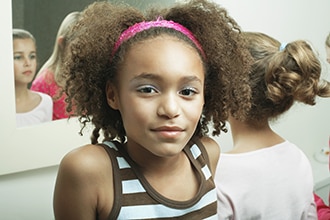 A preteen girl is at a bathroom mirror with her friends.