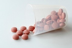 Clear cup of nonsteroidal anti-inflammatory drugs (NSAIDs) spilling out onto table.