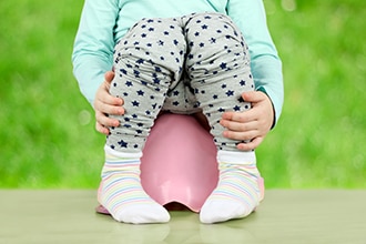 Si vedono le gambe di un bambino mentre si siede su un piccolo vasino.
