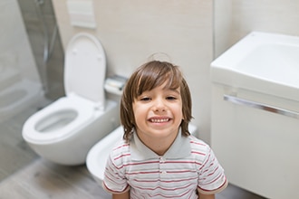 صبي يبتسم في الحمام مع مرحاض مفتوح في الخلفية.