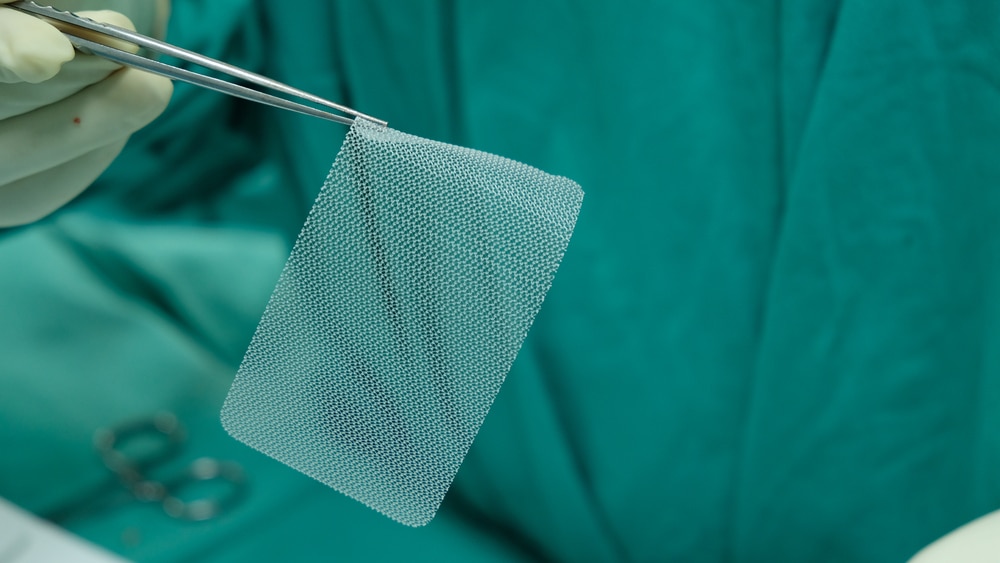 A surgeon using forceps to hold a piece of surgical mesh.