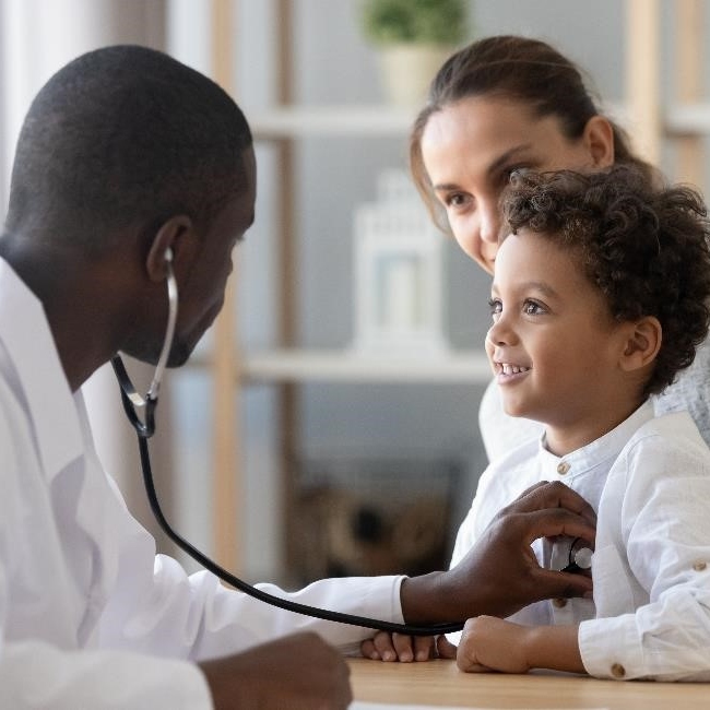 Mother holding child while a pediatrician listens to the child’s heart with a stethoscope.