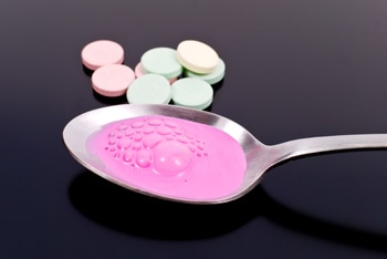 Photo of antacid tablets and spoon with antacid liquid.