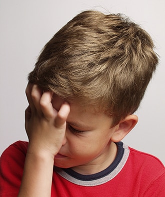 Young boy with eyes closed and hand pressed between his eyes.
