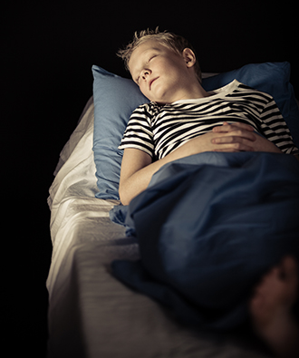 Young boy sleeping in a dark room.