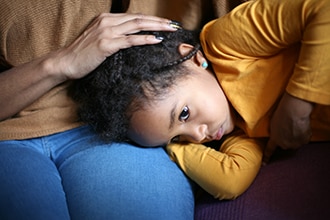 A sick girl lying on her mother’s lap.