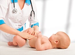 A health care professional examines an older infant’s belly.