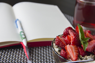 Bowl of strawberries on desk on top of a blank page of a journal book.