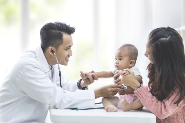 Médico con un estetoscopio escuchando los sonidos del abdomen de un bebé 