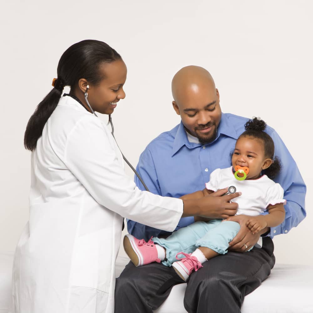 Health care professional examining a toddler who is being held by her father.