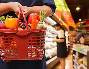 A person holding a grocery basket filled with vegetables.