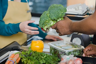 Shopper handing a bunch of broccoli to the checkout clerk at a grocery store