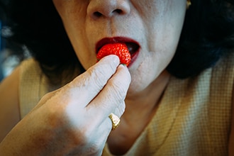 Una mujer se acerca una fresa a la boca para comérsela.