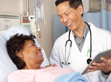 A doctor talking with a patient who is lying in a hospital bed.