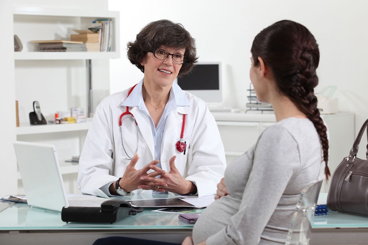 A female doctor sitting at a desk talking with a pregnant woman.