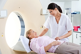 A CT scan machine, a health care provider, and a woman lying on a table for the CT scan.