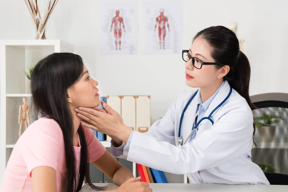 Female doctor examining a young woman’s neck.