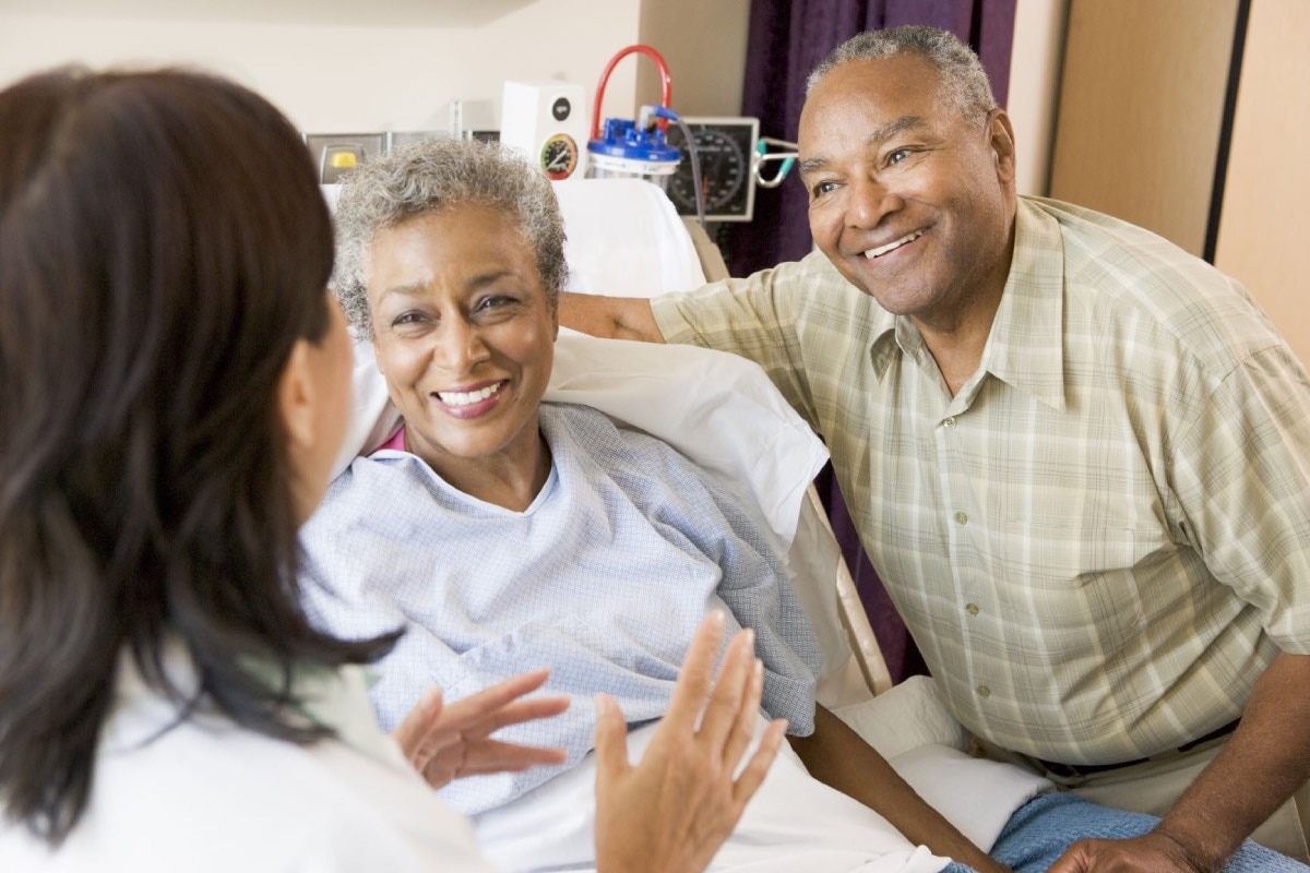 A smiling female patient and her spouse talking with her doctor in the hospital.