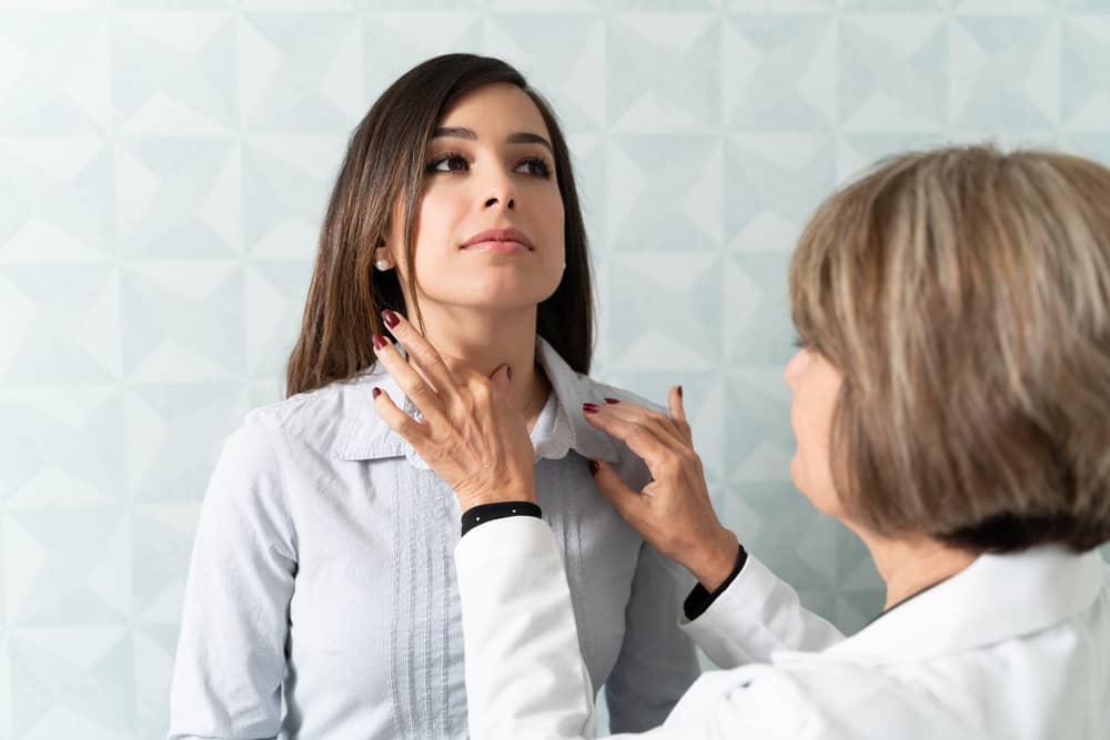 Female doctor examining a young woman’s neck.