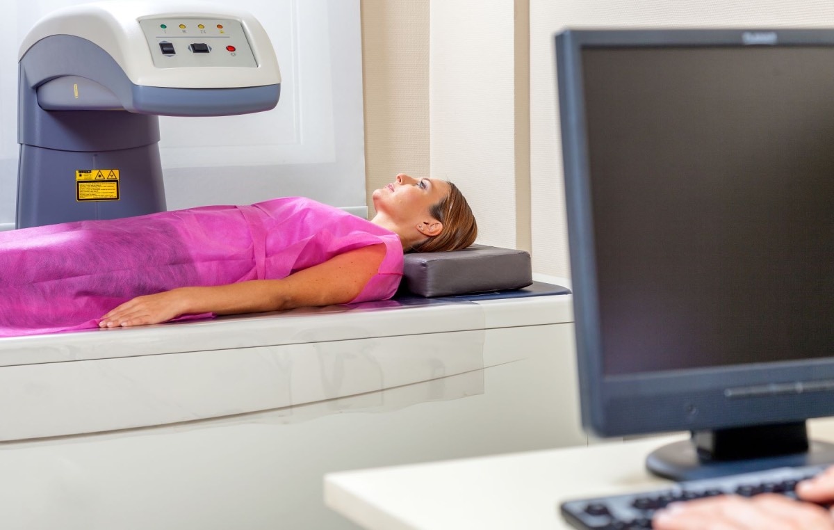 A woman lying on a table with a DXA scanner positioned over her abdomen.