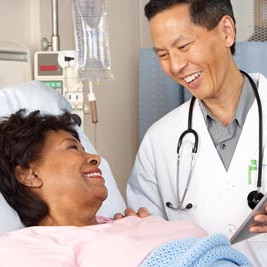 Un médico hablando con una paciente que está acostada en una cama de hospital.