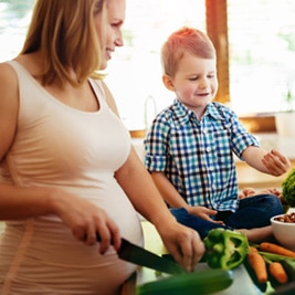 Pregnant woman preparing meal with son from fresh vegetables
