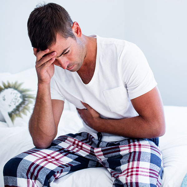 Man holding his stomach and head while sitting on a bed.