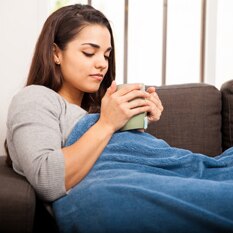 Woman under a blanket with a mug